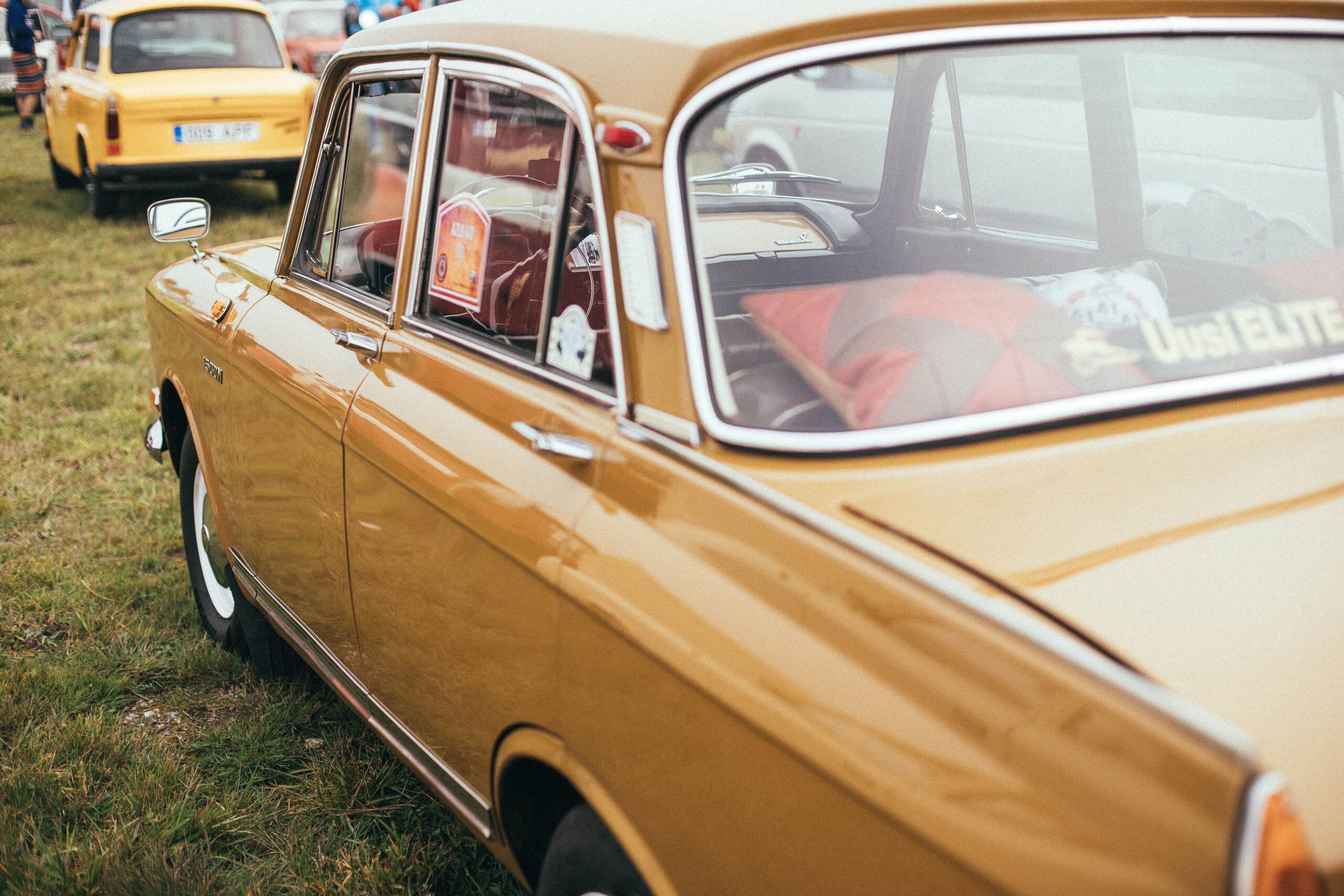 A classic yellow car parked on green grass, showcasing its vintage charm and side mirror reflections.